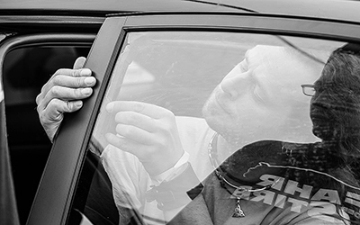 Nahaufnahme der Hände einer Person, die sorgfältig eine Folie an einem Seitenfenster eines Autos anbringt, mit Spiegelungen im Glas.